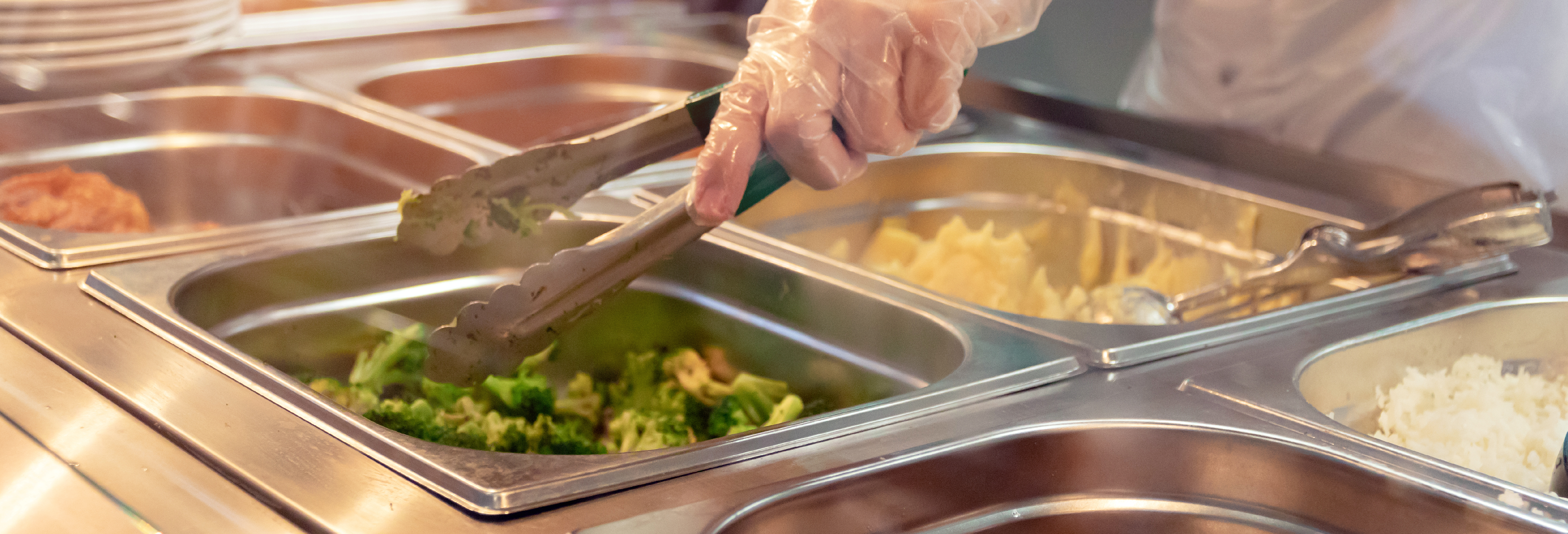 Mano con guanto che impugna un utensile che prendere il cibo in mensa 