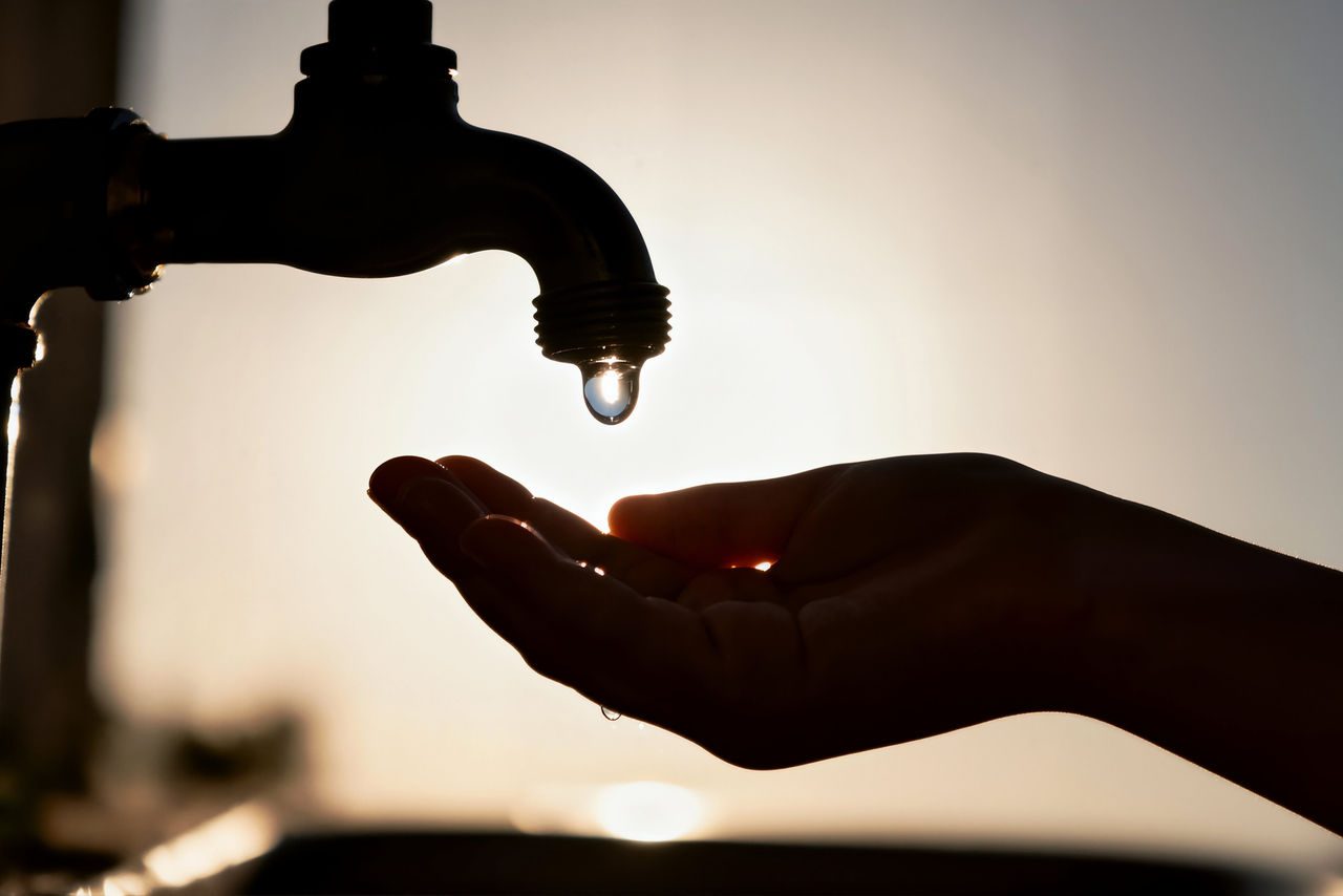 goccia d'acqua dal rubinetto alla mano sagomata