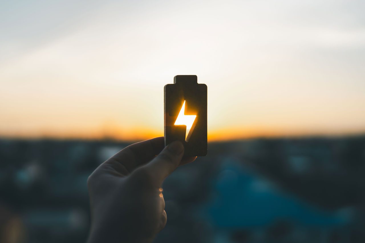 Mano che tiene in mano una batteria con dietro un tramonto