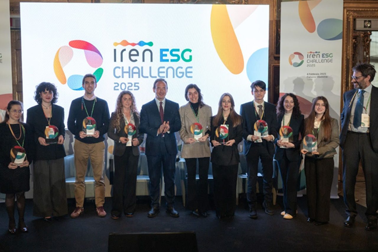 Un gruppo di giovani vincitori posa con i loro premi sul palco dell'Iren ESG Challenge 2025. Dietro di loro, un grande schermo mostra il logo dell'evento con scritte colorate.