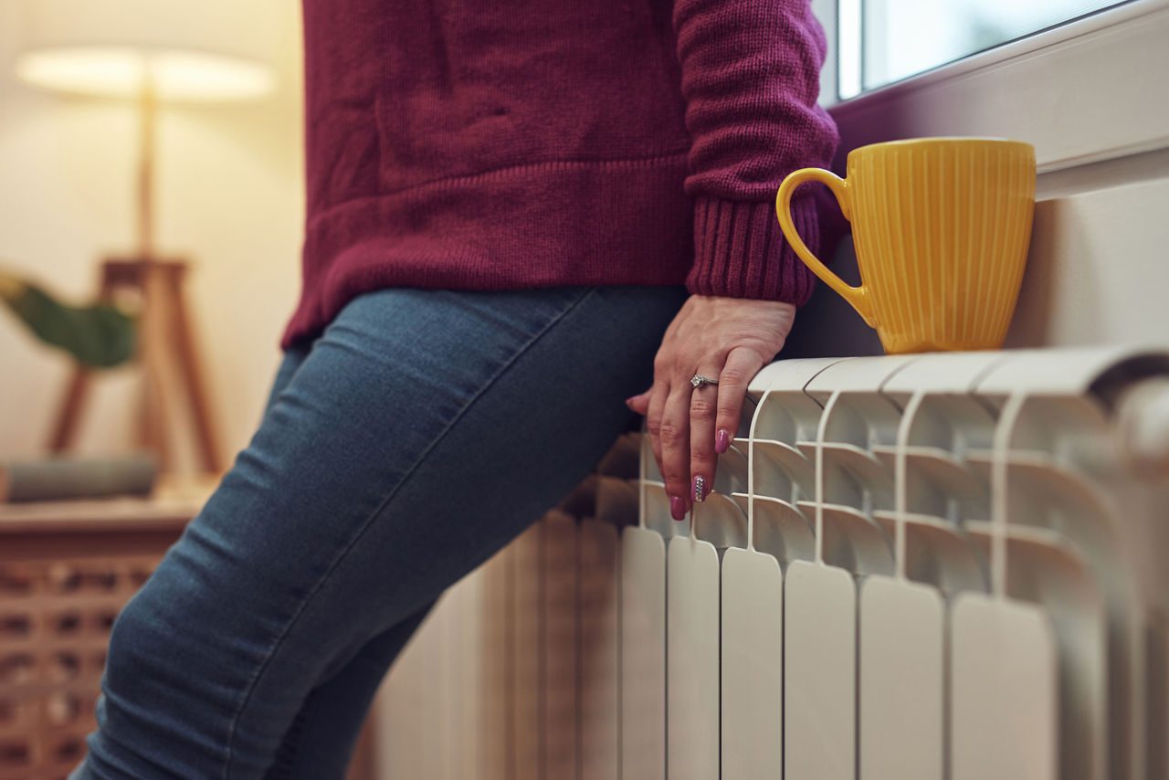 donna appoggiata al termosifone con una tazza gialla sopra