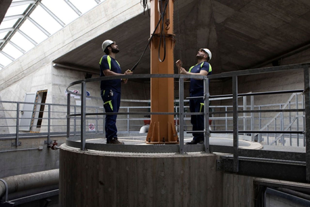 Due operai con casco e divisa da lavoro che controllano un impianto idrico all'interno di una struttura industriale.