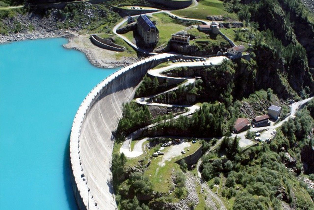 Veduta aerea di una diga idroelettrica in montagna con lago turchese.