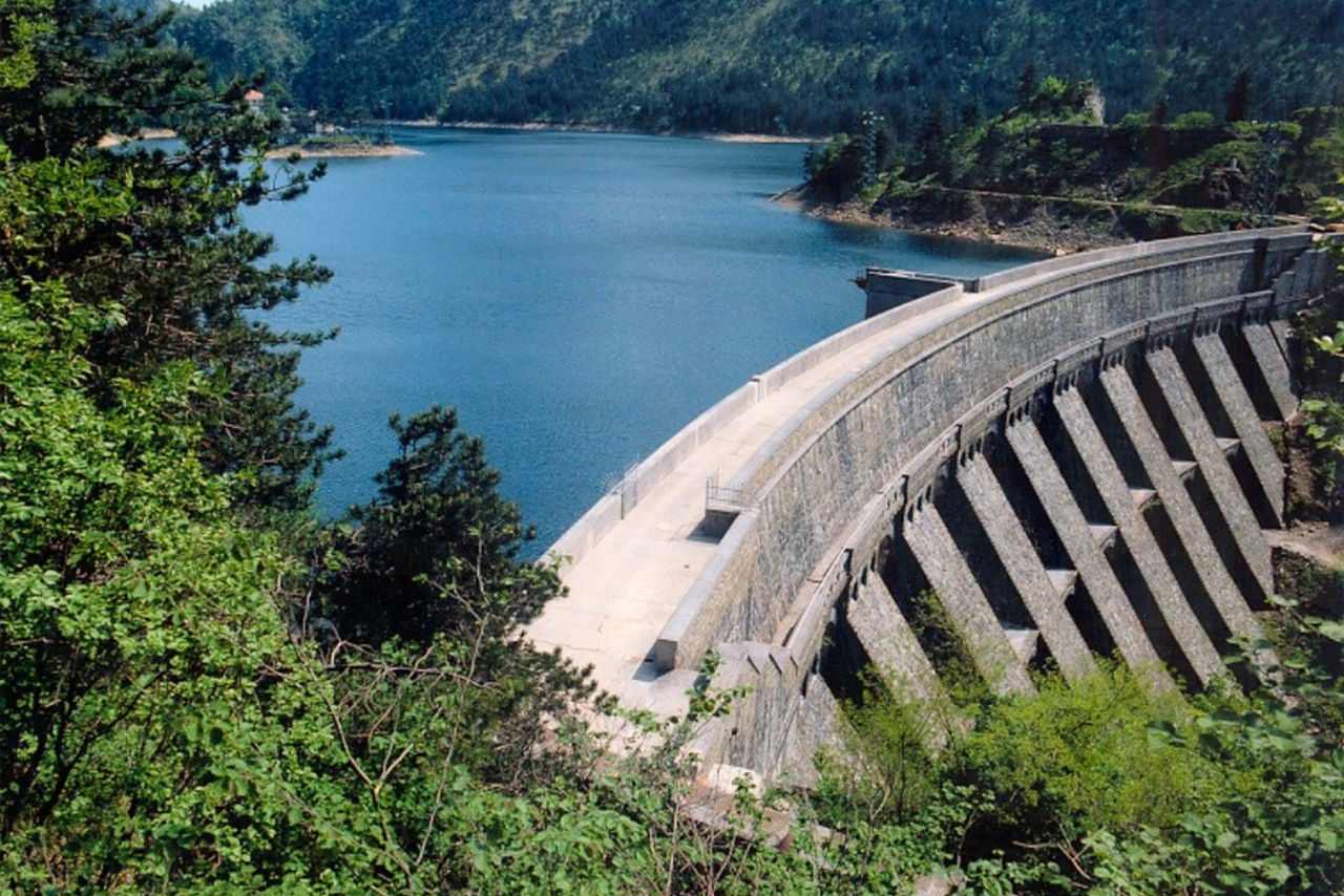 Veduta aerea di una diga idroelettrica in montagna con lago turchese.