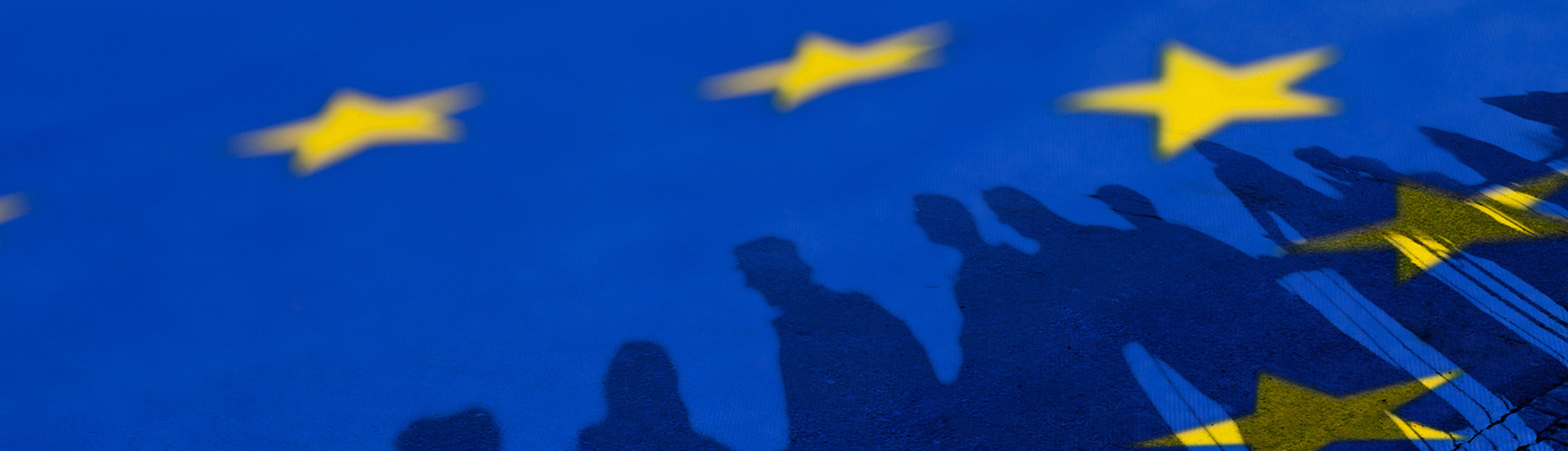 Bandiera dell'Unione Europea con silhouette di persone in primo piano, simbolo di coesione e impegno collettivo verso obiettivi comuni.
