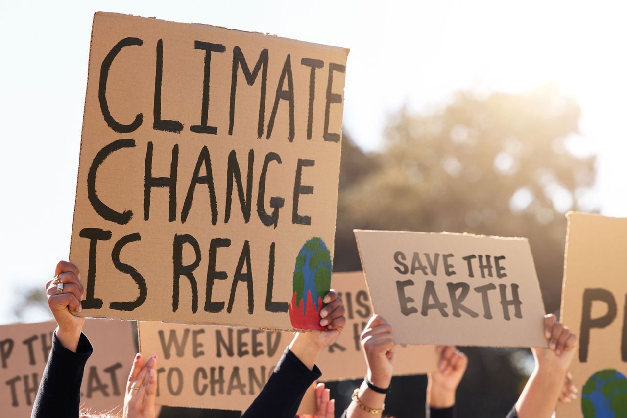 Persone sollevano cartelli durante una manifestazione per il clima con scritte come “Climate change is real” e “Save the Earth”, a sostegno della lotta contro il cambiamento climatico.