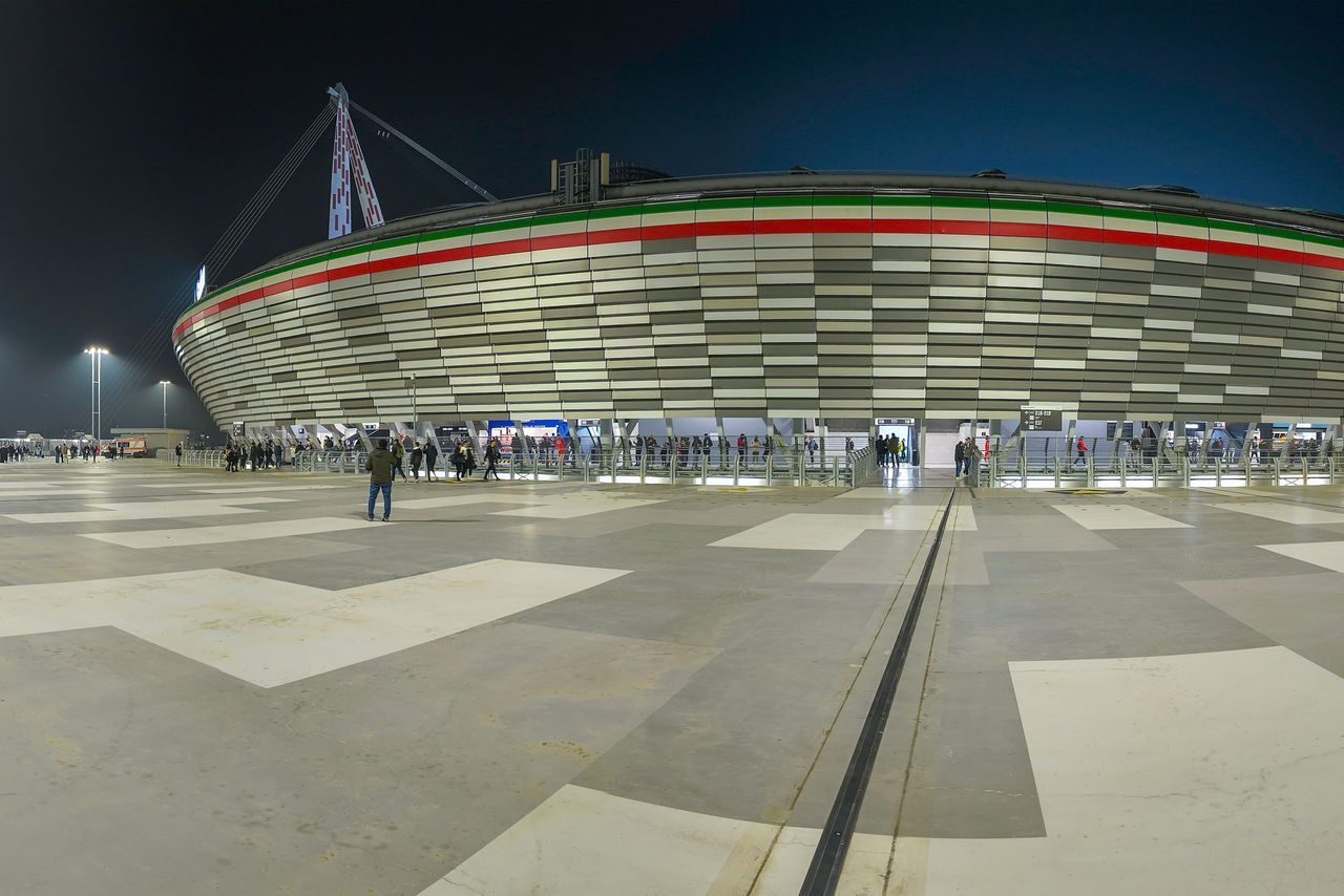 Veduta serale dell’Allianz Stadium di Torino con persone all’ingresso e la facciata illuminata dai riflessi delle luci artificiali.