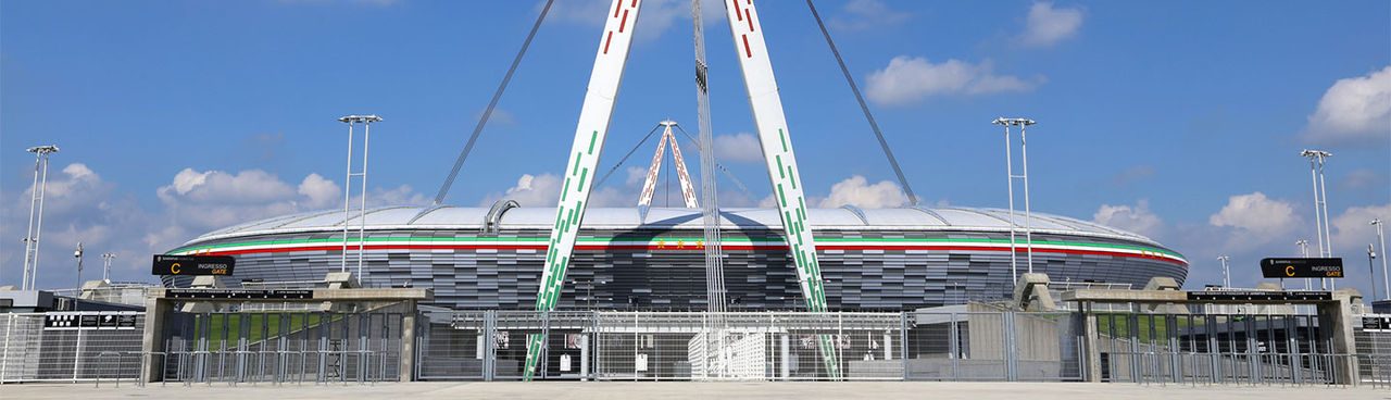 Vista frontale dell’Allianz Stadium di Torino, con la struttura moderna e gli iconici piloni bianchi decorati con linee rosse e verdi.