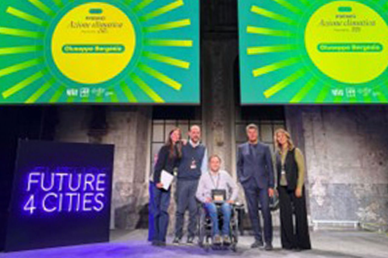 Un gruppo di sei persone in posa sul palco dell’evento Future4Cities, con due grandi schermi verdi alle spalle che mostrano il nome del premio e il vincitore. In primo piano, l’insegna luminosa “Future 4 Cities”.