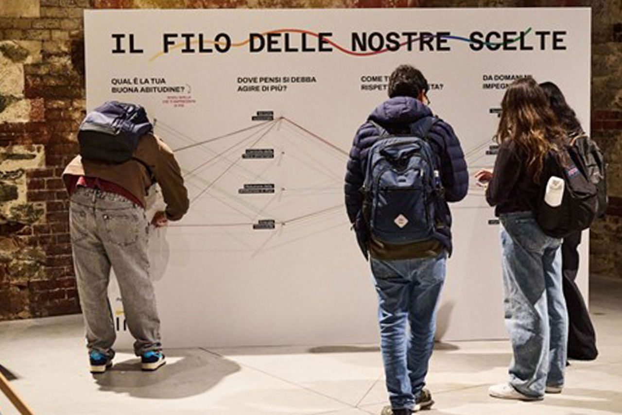 Tre giovani osservano e interagiscono con una parete espositiva intitolata “Il filo delle nostre scelte”, che propone un percorso di riflessione su sostenibilità e impegno individuale attraverso domande e collegamenti.