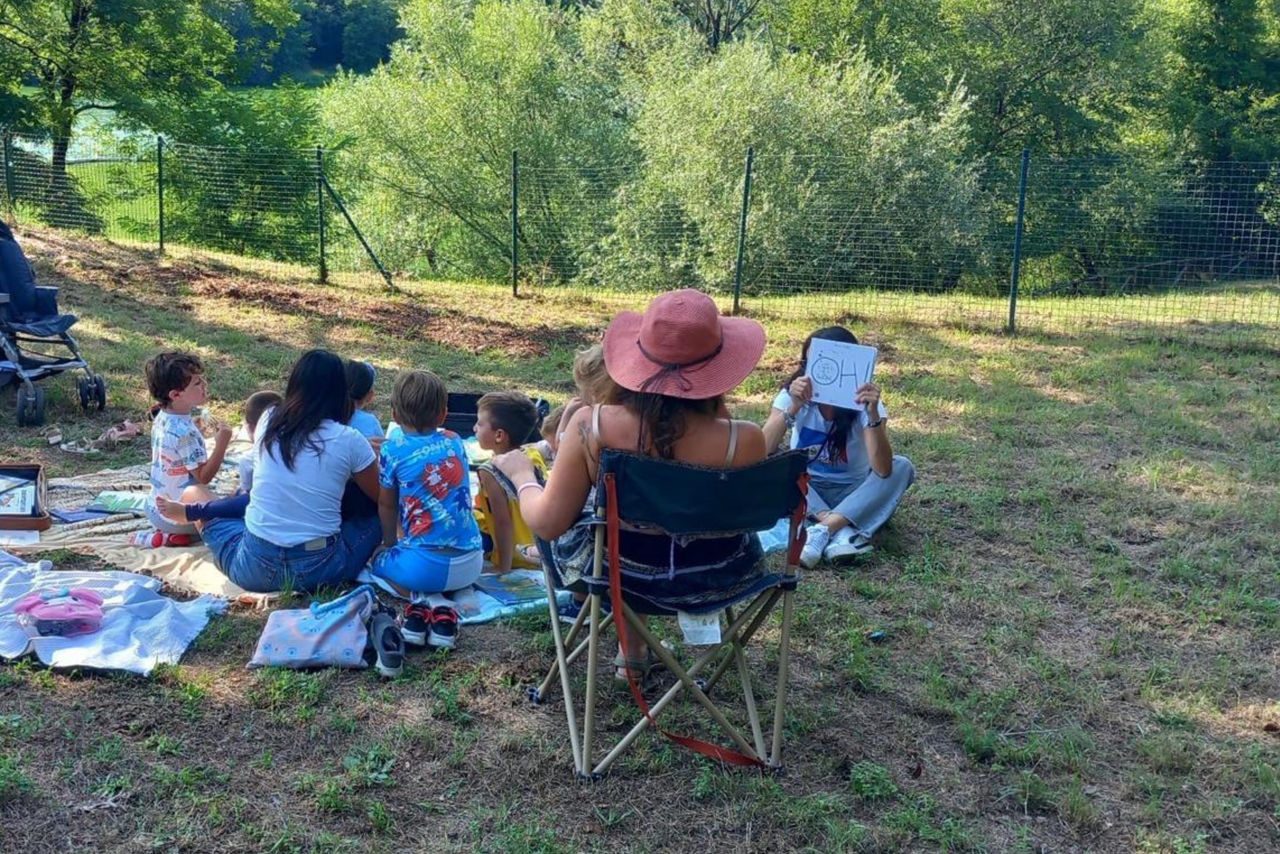 bambini e bambine tutti insieme seduti sul prato, che giocano e imparano in un verde giardino