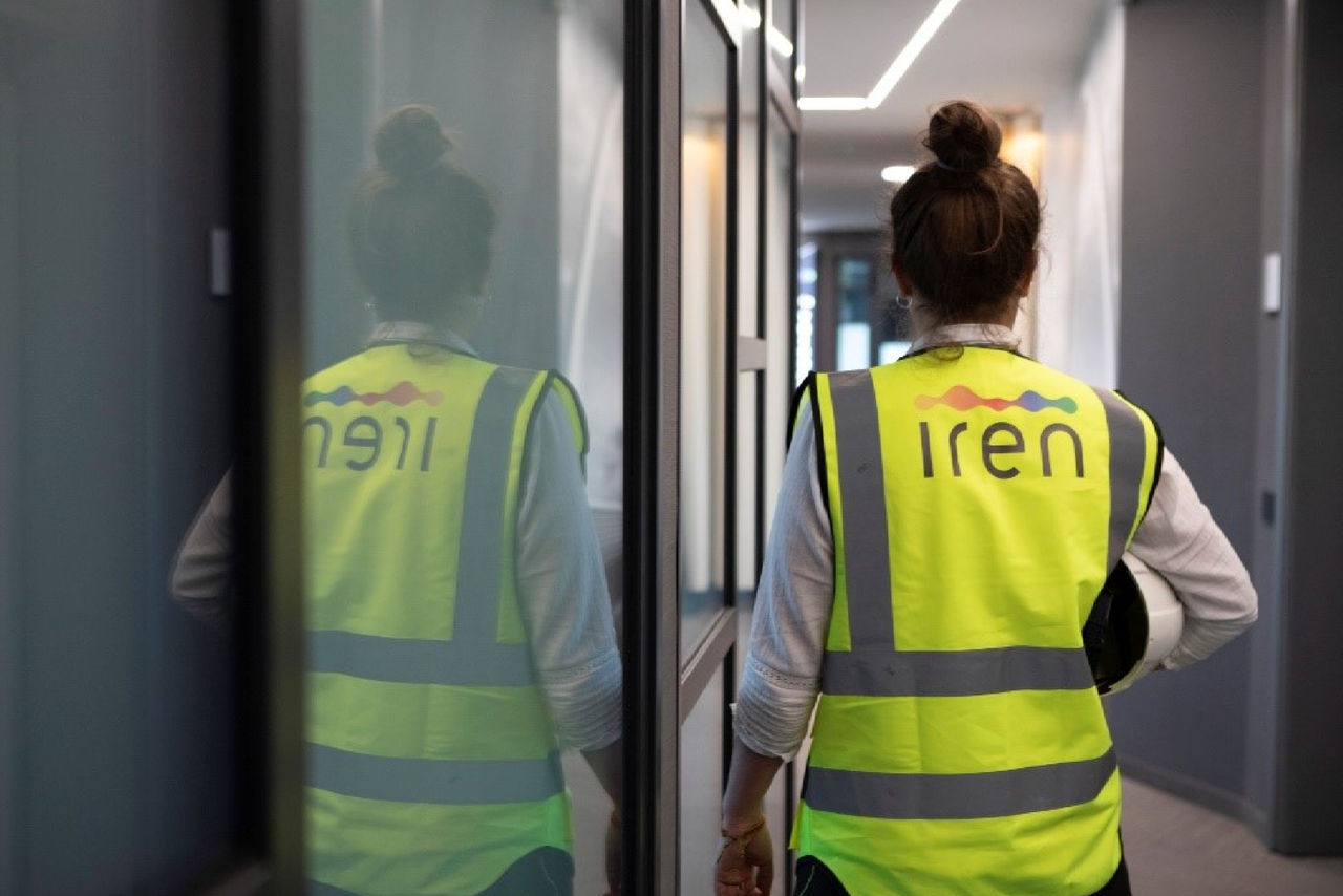 ingegnera Iren di spalle con pettorina e caschetto in corridoio di uffici