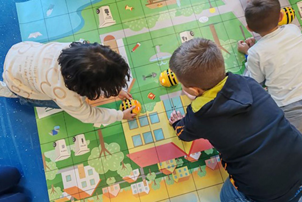 Bambini giocano con gioco a forma di ape su una mappa illustrata a griglia, durante un’attività educativa interattiva sulla sostenibilità.