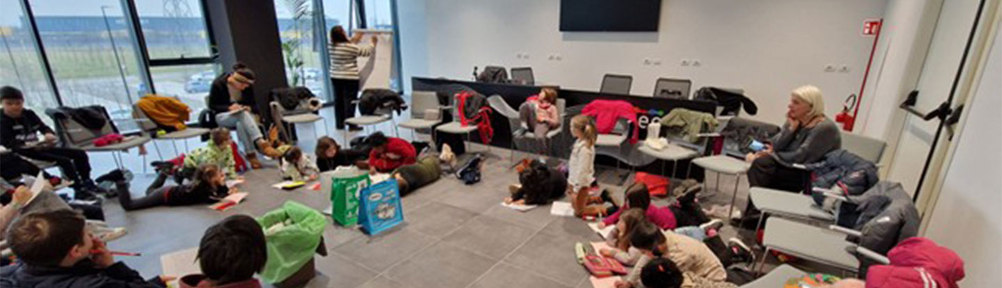 Attività di educazione ambientale in aula con bambini seduti a terra che disegnano, guidati da educatrici.