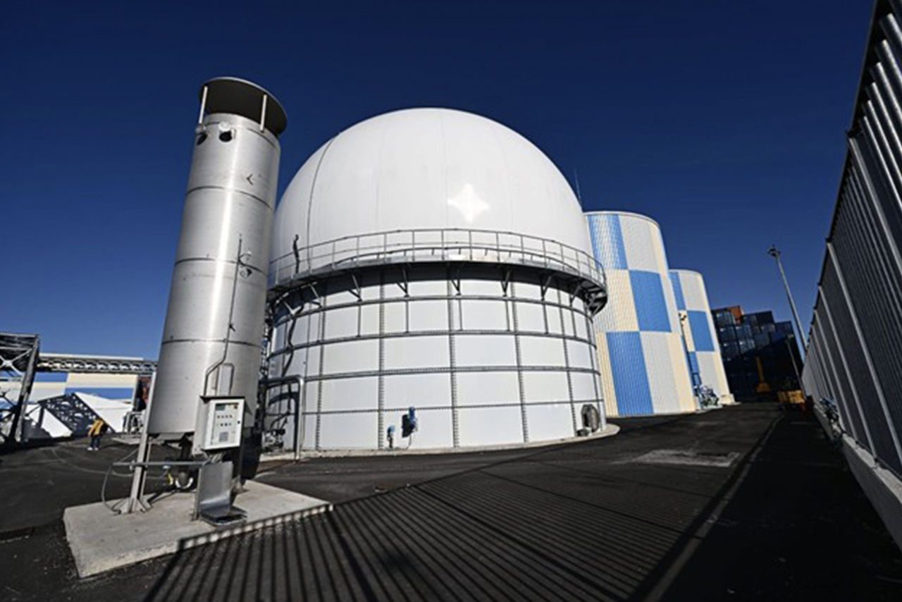 Struttura industriale con serbatoi e impianti tecnologici all’aperto, caratterizzata da una grande cupola bianca e cisterne metalliche sotto un cielo sereno.