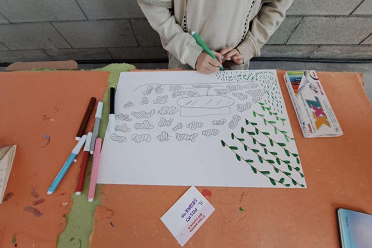 Bambina che colora un foglio decorato con disegni di pesci e foglie durante un laboratorio creativo.