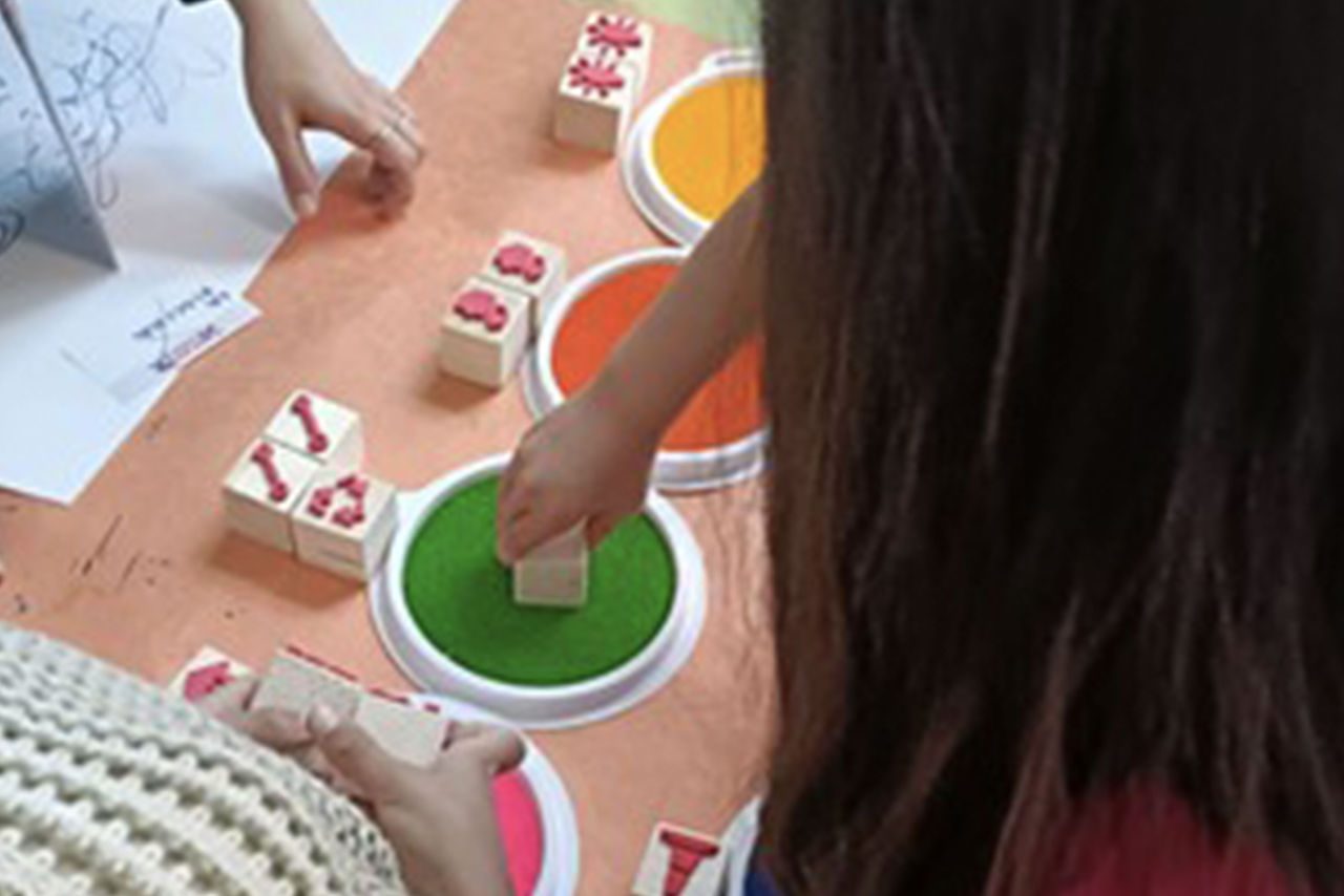 Bambini intenti a utilizzare timbri colorati su un tavolo arancione durante un'attività creativa.