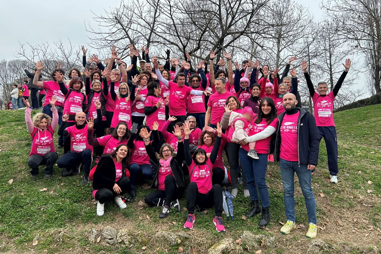 Gruppo di persone sorridenti con magliette rosa che partecipano all'evento di beneficenza "Just the Woman I Am", riuniti su una collina erbosa.