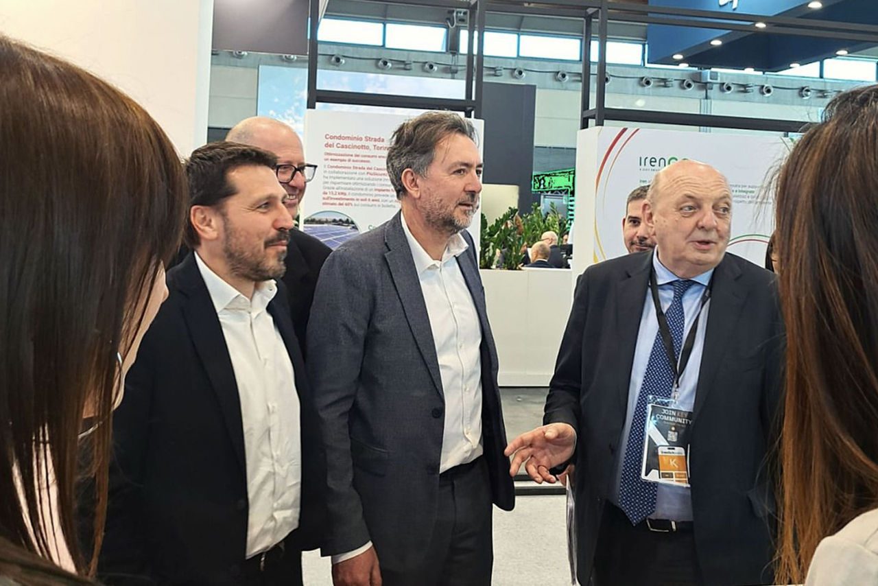 Delegazione di uomini in giacca e cravatta in visita allo stand di Iren durante Key Energy 2025, tra cui il ministro dell’Ambiente e della Sicurezza Energetica, Gilberto Pichetto Fratin. Uno di loro gesticola mentre dialoga con lo staff.