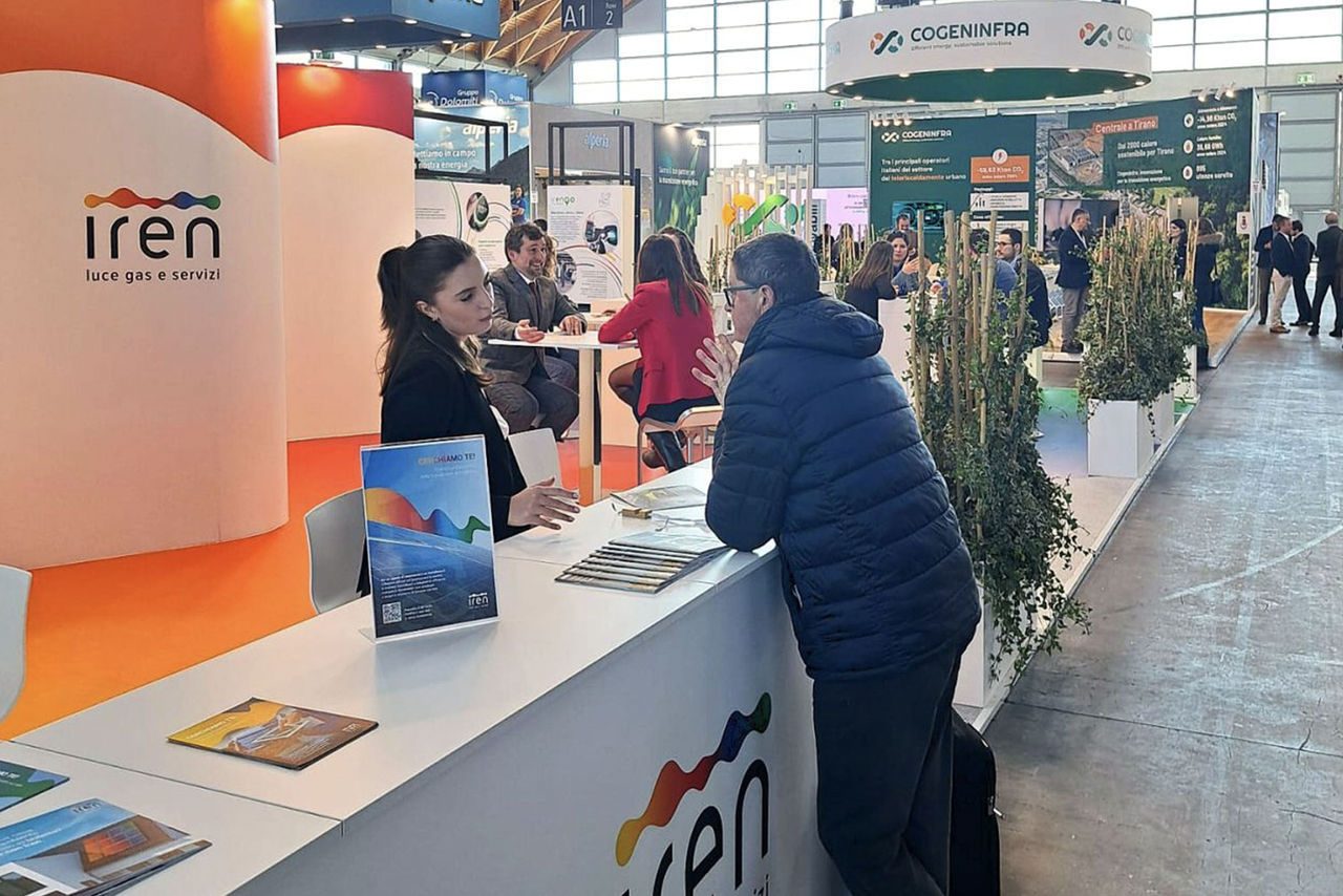 Stand di Iren a Key Energy 2025, con un'area espositiva moderna caratterizzata da pannelli arancioni e bianchi con il logo aziendale. Un operatore fornisce informazioni a un visitatore presso il bancone dell’accoglienza.