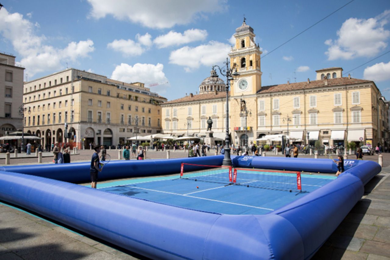 Campo da tennis gonfiabile in Piazza Garibaldi a Parma, con sfondo di edifici storici e cielo azzurro.
