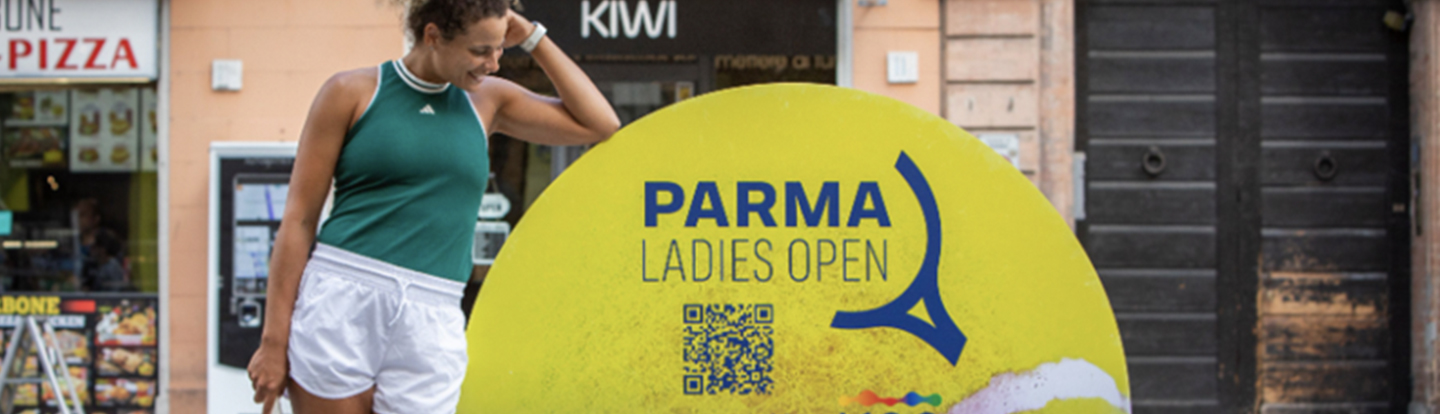 Tennista posa sorridente accanto all’insegna del torneo “Parma Ladies Open presented by Iren”, in centro città.
