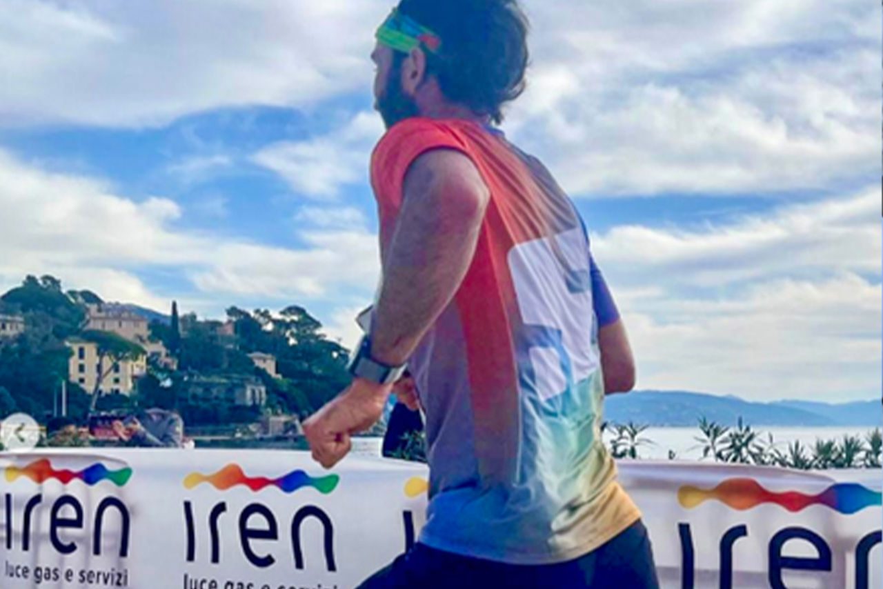 Un corridore con maglietta colorata e fascia sportiva attraversa il traguardo della Portofino Marathon, con banner di Iren visibili lungo il percorso.