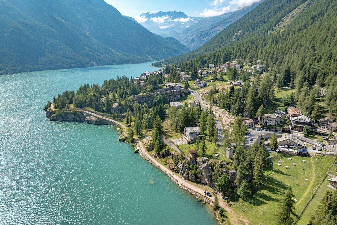 Veduta panoramica di un lago alpino con paesino immerso tra le montagne e i boschi.