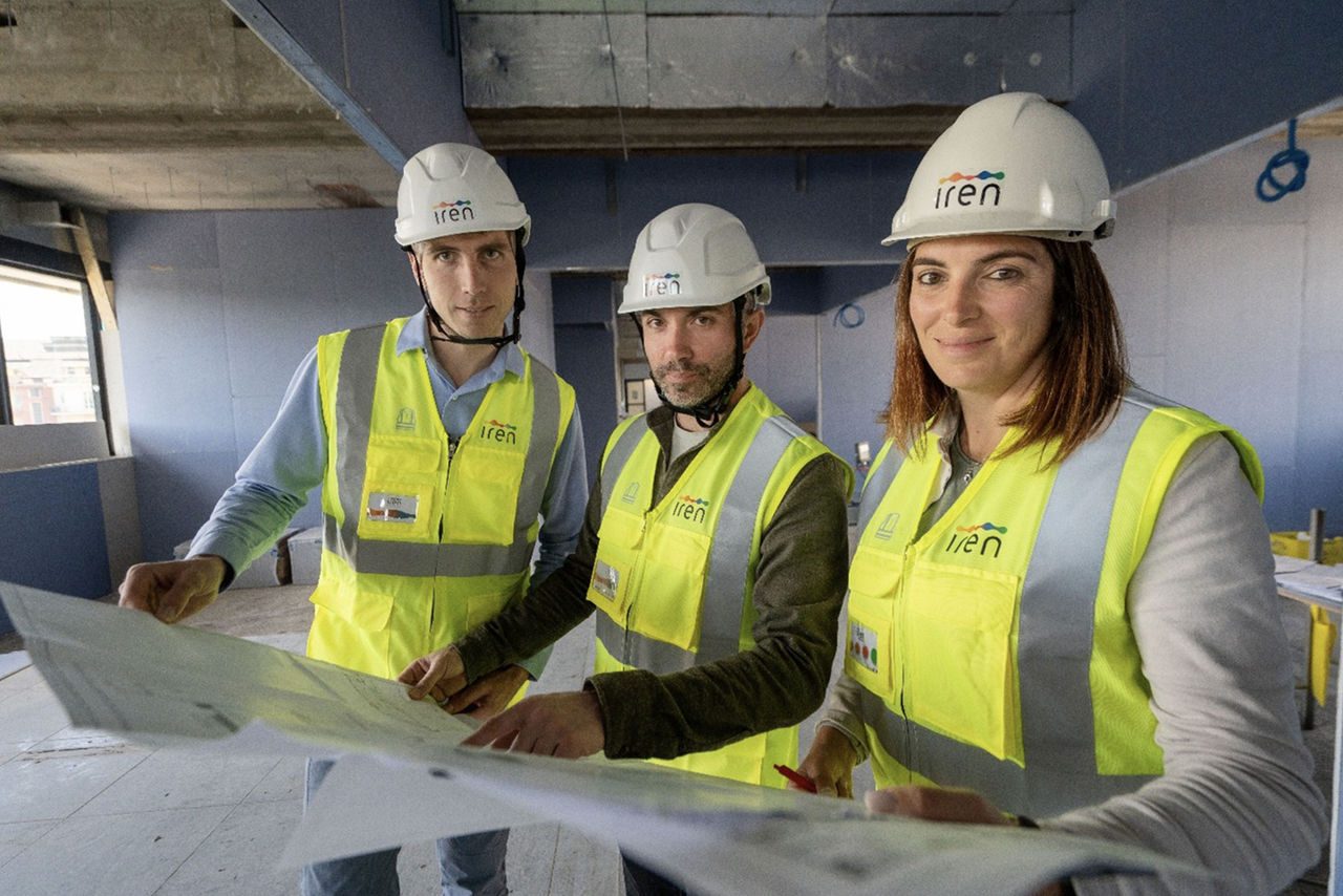 Tre tecnici Iren con caschetto e gilet ad alta visibilità esaminano dei progetti all’interno di un cantiere in fase di costruzione.