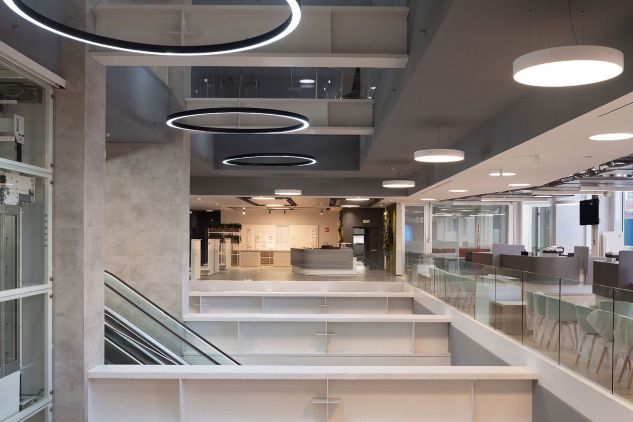 Interno moderno di un edificio con illuminazione circolare a soffitto e scala mobile, caratterizzato da un design elegante e spazi ampi.
