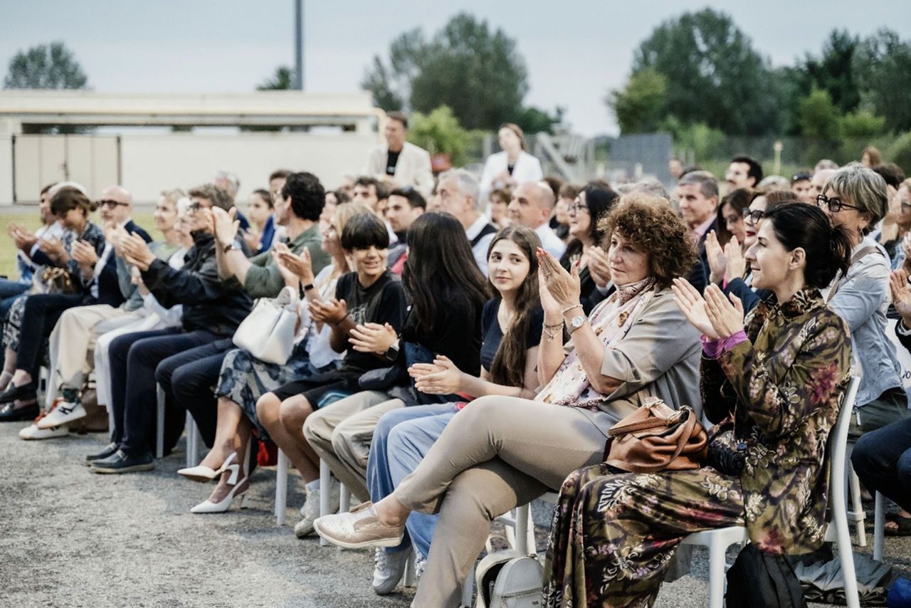 Primo piano del pubblico durante un evento culturale all’aperto: le persone applaudono sorridendo, sedute in prima fila davanti al palco allestito presso l’impianto TRM.