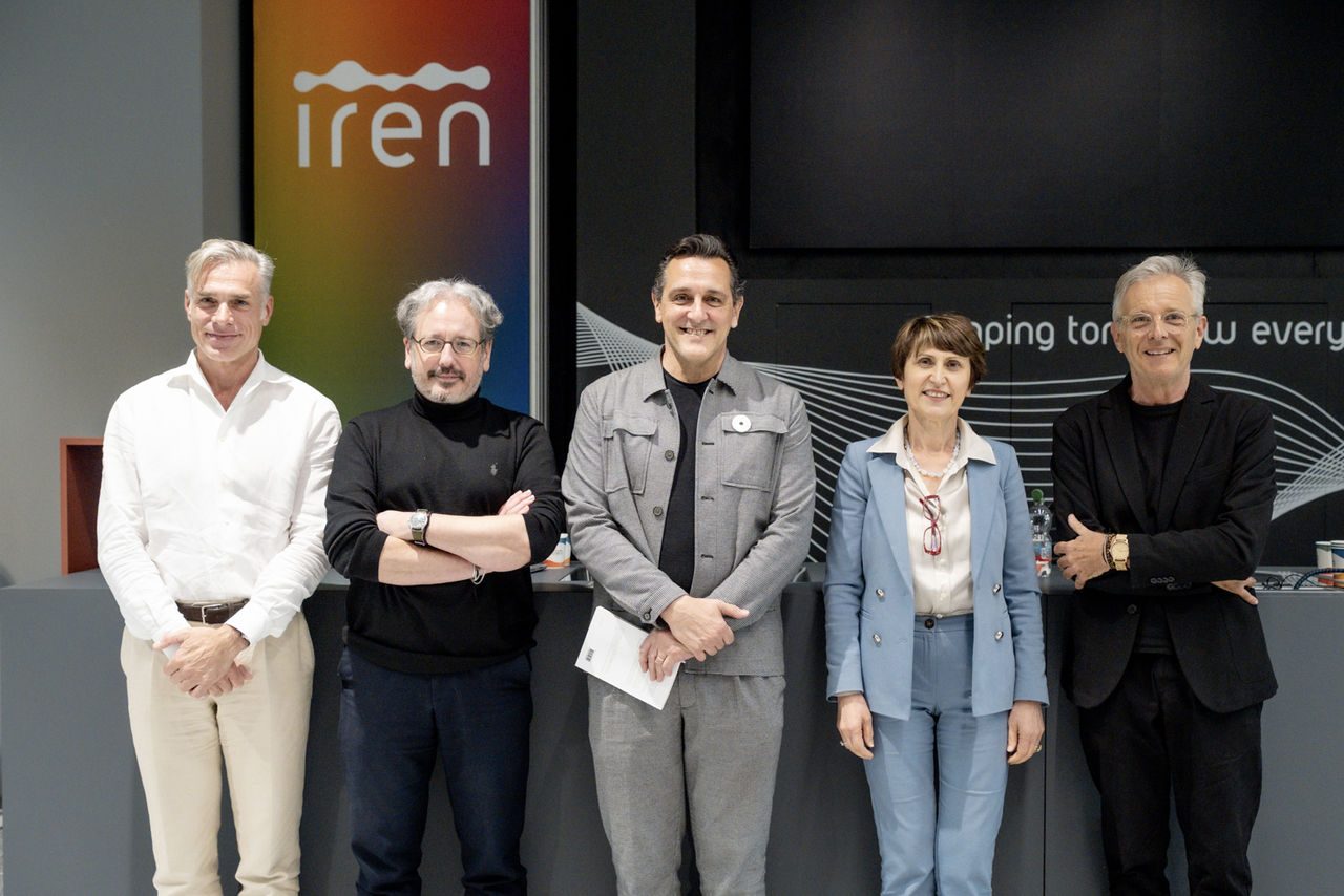 Cinque relatori in posa davanti al logo Iren dopo un evento, su sfondo nero con decorazioni grafiche bianche e scritta “Shaping tomorrow everyday”.