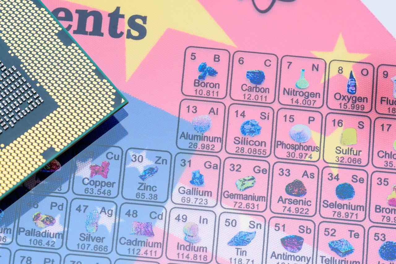 Primo piano di un microchip appoggiato su una tavola periodica con evidenziati elementi chimici critici come silicio, gallio e litio.