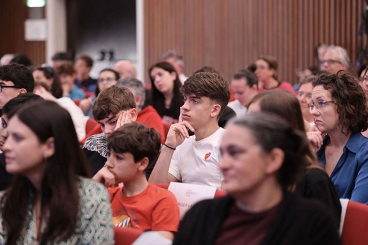 Ragazzi e adulti seduti in platea seguono con concentrazione l’evento.