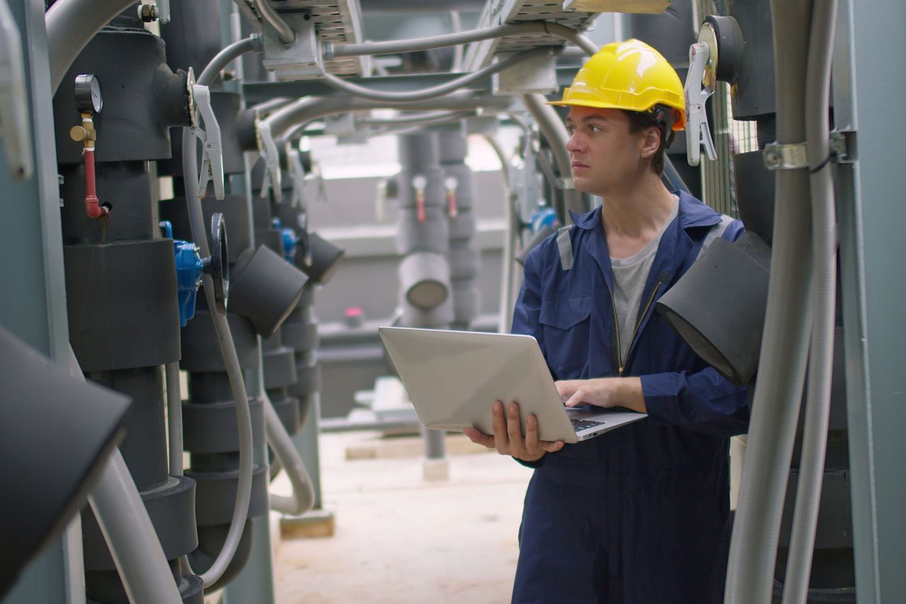 ingegnere che gestisce un computer portatile in un complesso impianto industriale