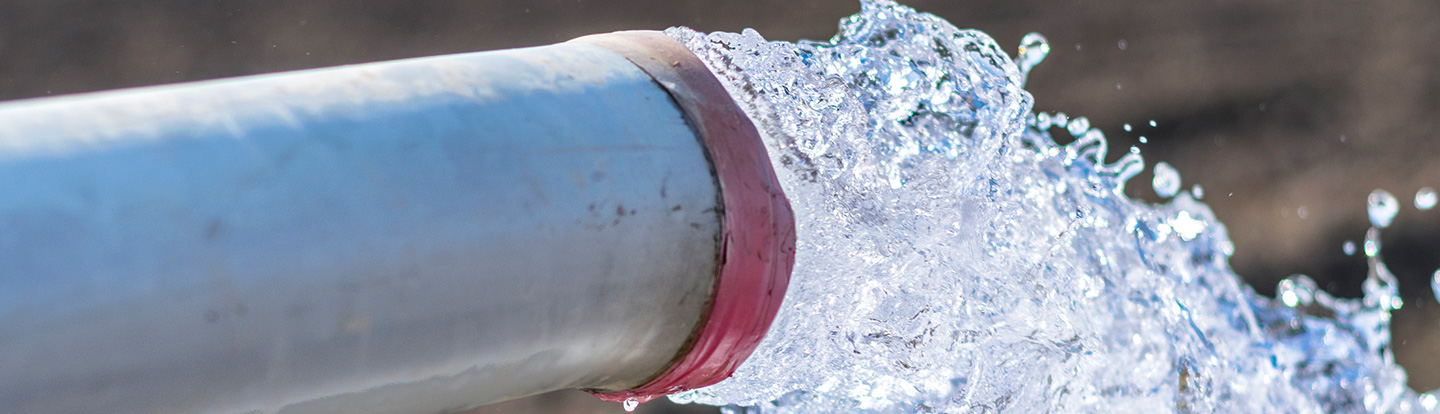 Flusso d’acqua potabile che sgorga da un tubo industriale pesante posizionato a terra, simbolo della distribuzione idrica in ambito urbano.