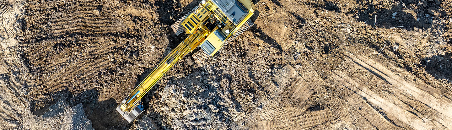 Immagine aerea di un escavatore al lavoro in un cantiere, che sposta terra e detriti