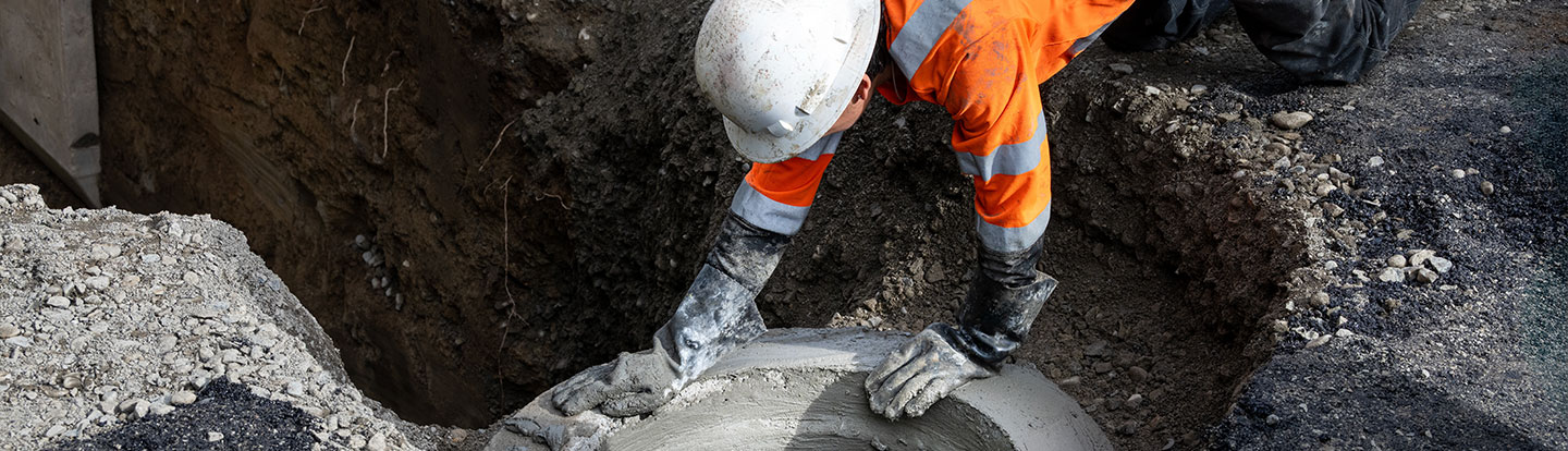 lavoratore edile che installa un anello di cemento prefabbricato al punto di accesso al foro di servizio per il nuovo progetto di installazione di infrastrutture per il sistema fognario pubblico