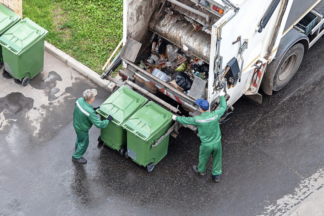 due netturbini dietro un autocarro autocompattatore che stanno per svuotare due secchioni verdi della spazzatura