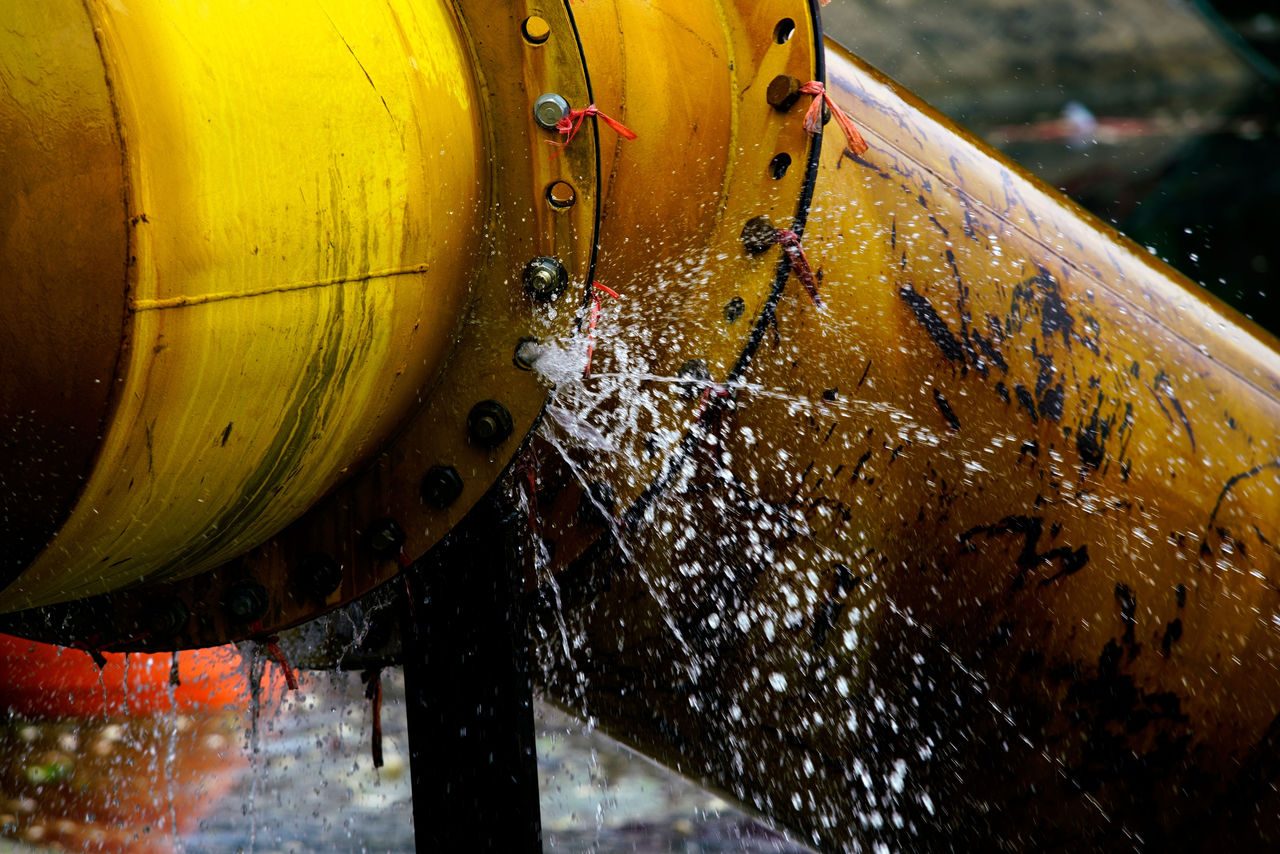Un tubo industriale giallo con evidenti problemi meccanici nelle infrastrutture e perdita d'acqua