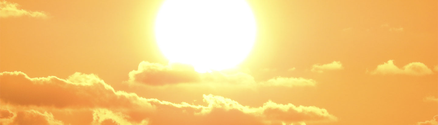Il sole splende in un cielo completamente arancione con alcune nuvole chiare in primo piano, evocando un’intensa ondata di calore.