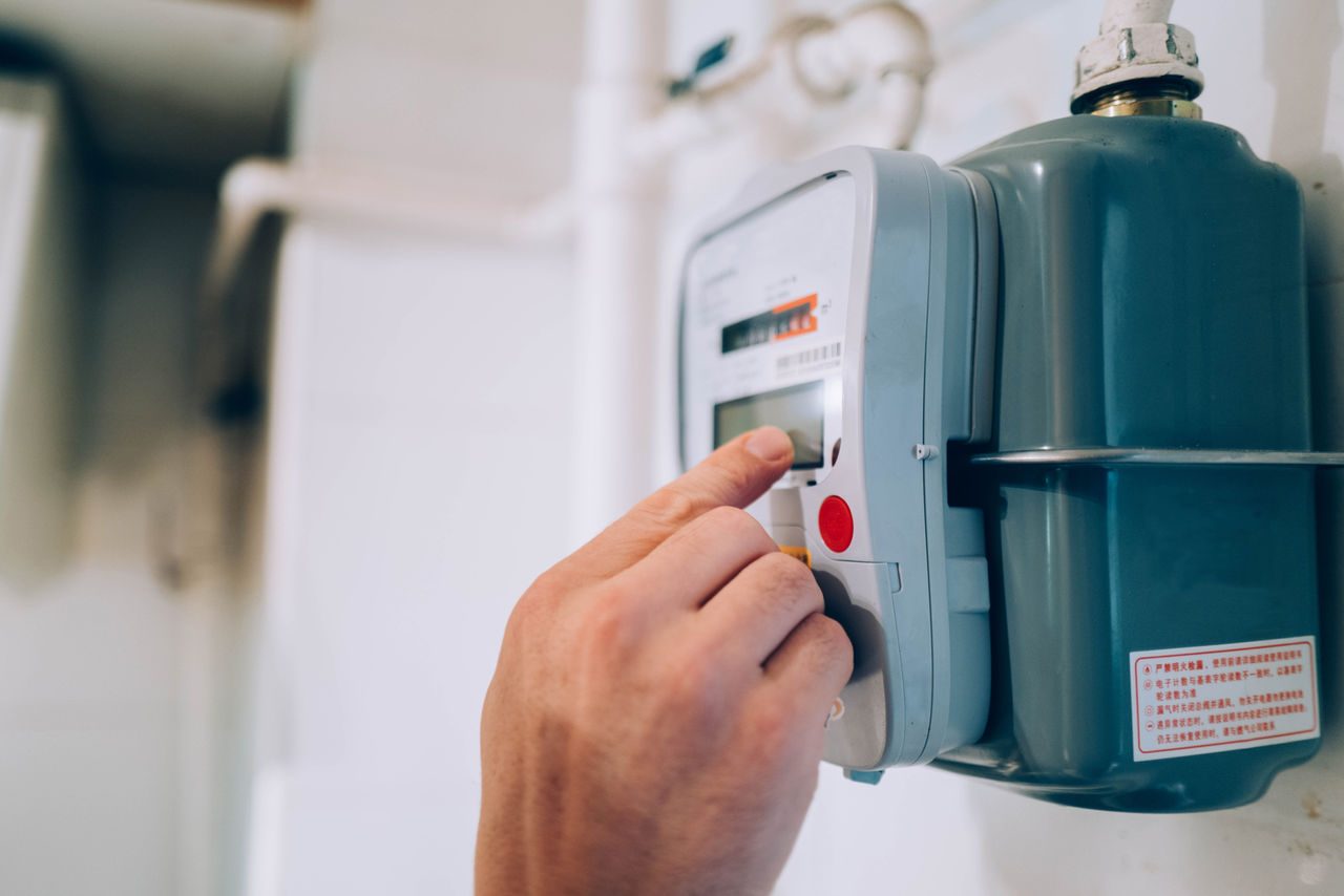 Primo piano di una mano e sullo sfondo un contatore per l'energia elettrica. 