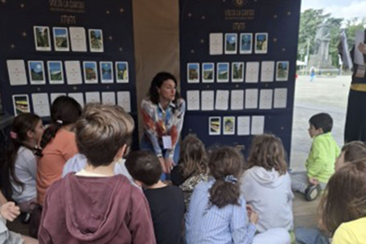 Una facilitatrice parla a un gruppo di bambini seduti su cuscini, con un cane disteso tra loro.
