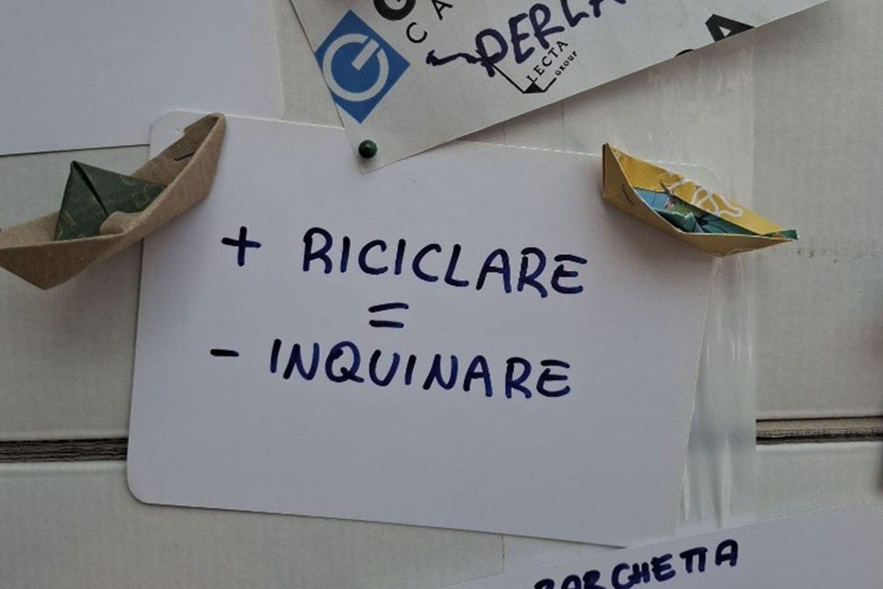 Primo piano di cartoncini con frasi come “+ riciclare = - inquinare” e origami colorati.