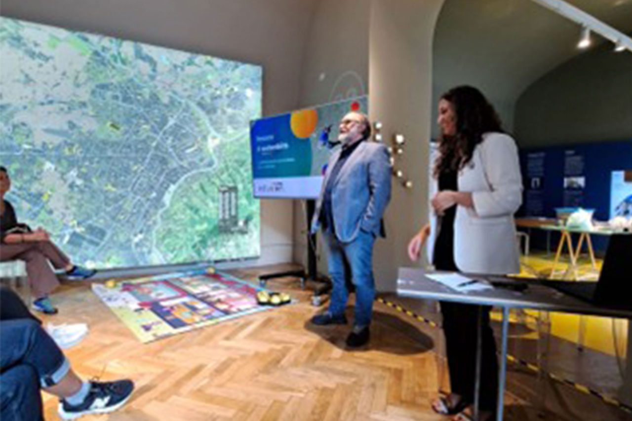 Presentazione interattiva in uno spazio espositivo Eduiren, con proiezione di una mappa e robot didattici a terra, davanti a un gruppo di partecipanti.