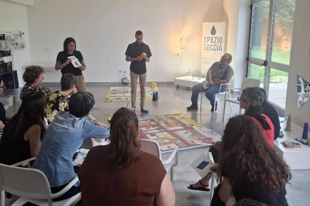 Attività educativa in aula: un facilitatore mostra materiali didattici a un gruppo di adulti seduti in cerchio, nello spazio Spazio Goccia.