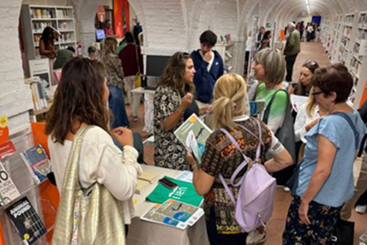 Momento di dialogo tra educatrici e visitatori durante un evento Eduiren all’interno di una biblioteca, con tavolo espositivo e materiali didattici.