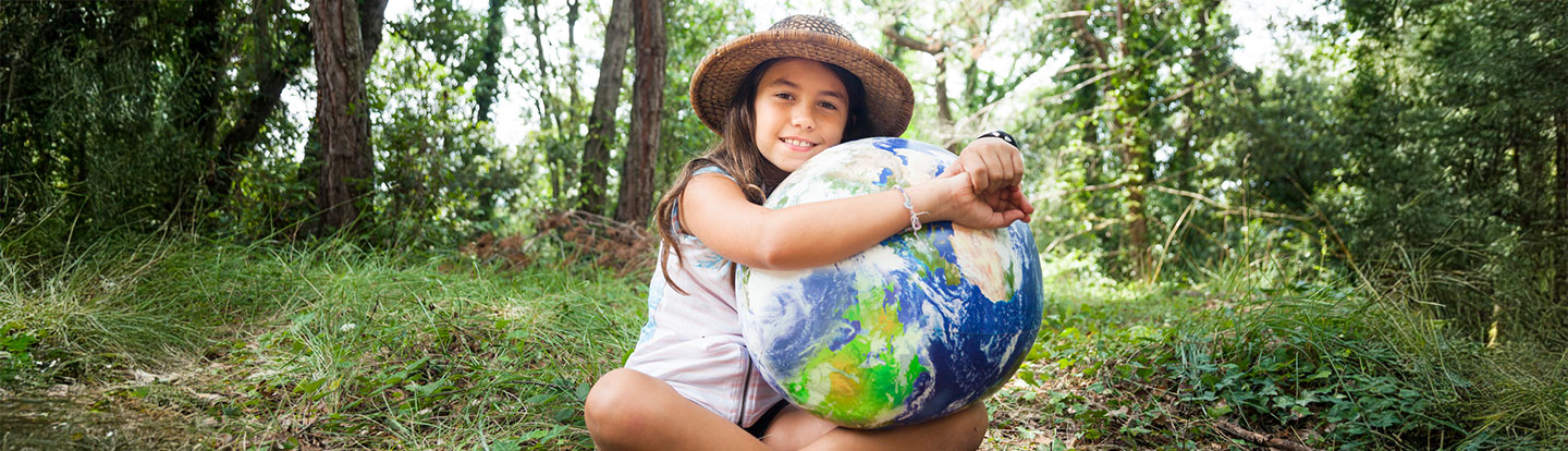 Bambina seduta su un prato verde che abbraccia un grande mappamondo, simbolo di amore per la Terra e sostenibilità ambientale.