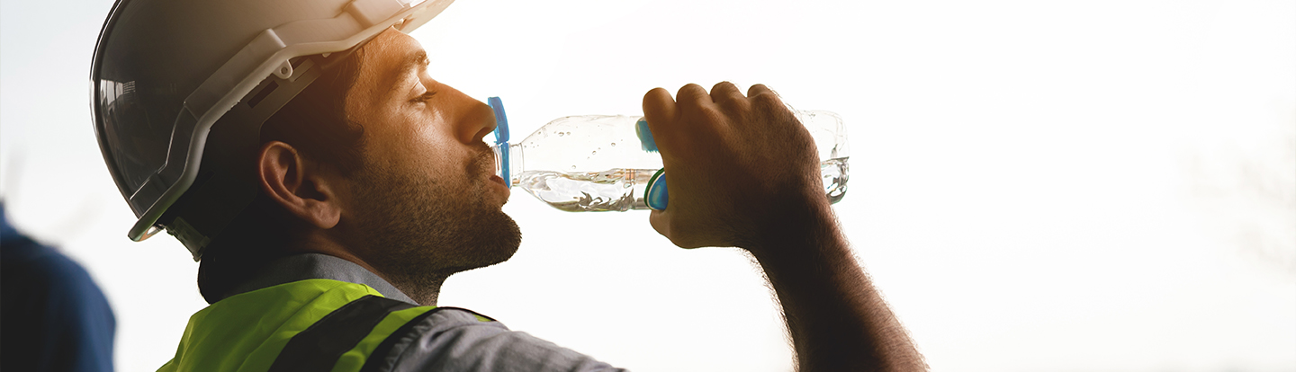 operaio con caschetto protettivo da cantiere che beve da una bottiglietta d'acqua