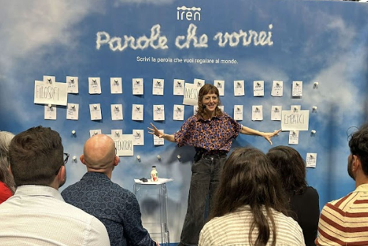 La giornalista Francesca Berardi su un palco davanti a un pubblico di spalle, durante un incontro del ciclo nello stand Iren "Parole che vorrei", con parete decorata da bigliettini contenenti parole ispirazionali.